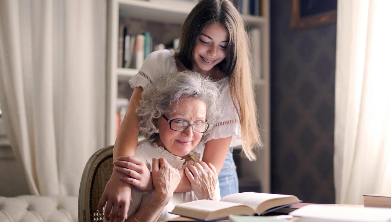 older woman reading a book with teenager looking on. 