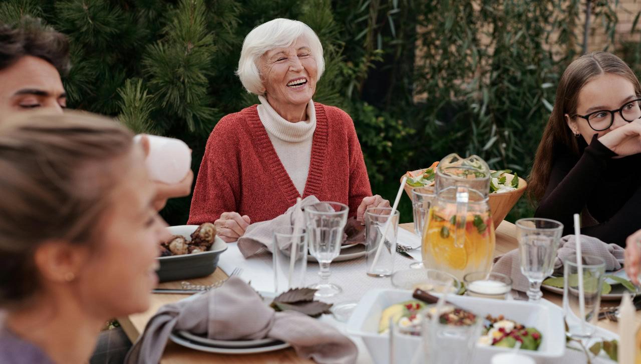 older woman sits at head of table at outdoor meal